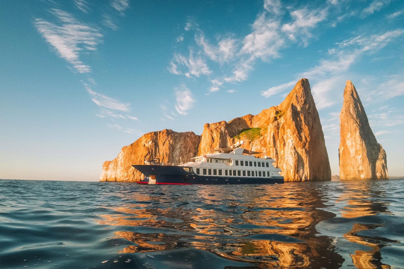 Small Galapagos cruise yacht sailing beside dramatic volcanic rock formations in the Galapagos Islands.